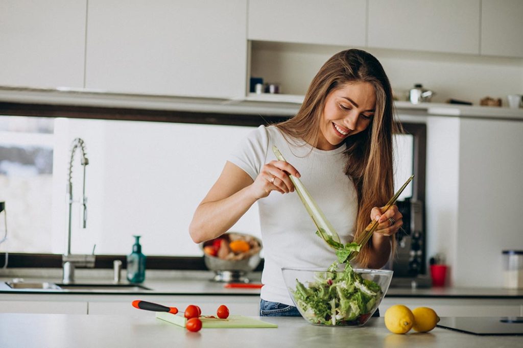 Jovem preparando salada como forma de manter a pele bonita